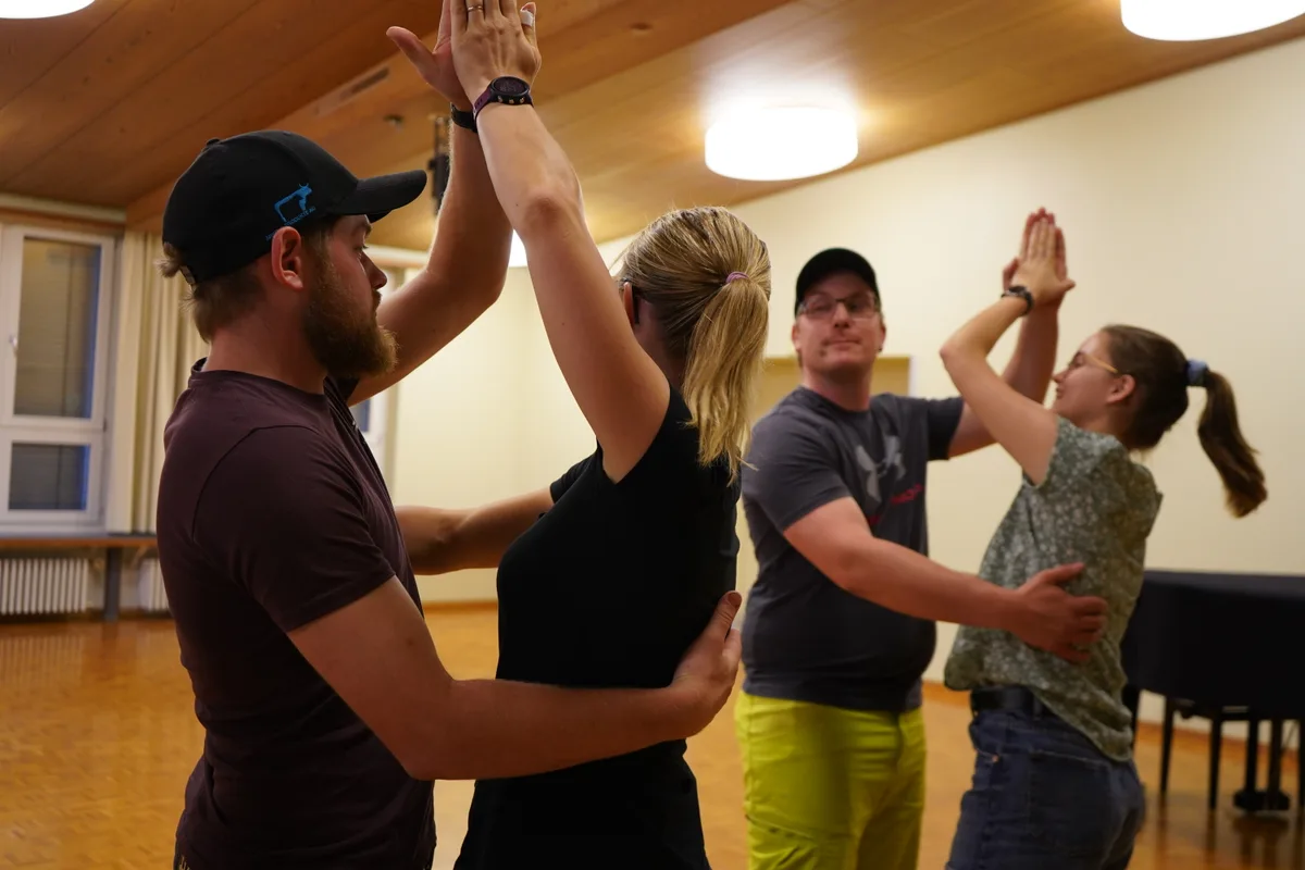 Zwei Tanzpaare machen die Türmlifigur: eine Hand umarmt den Partner, die andere ist über dem Kopf.